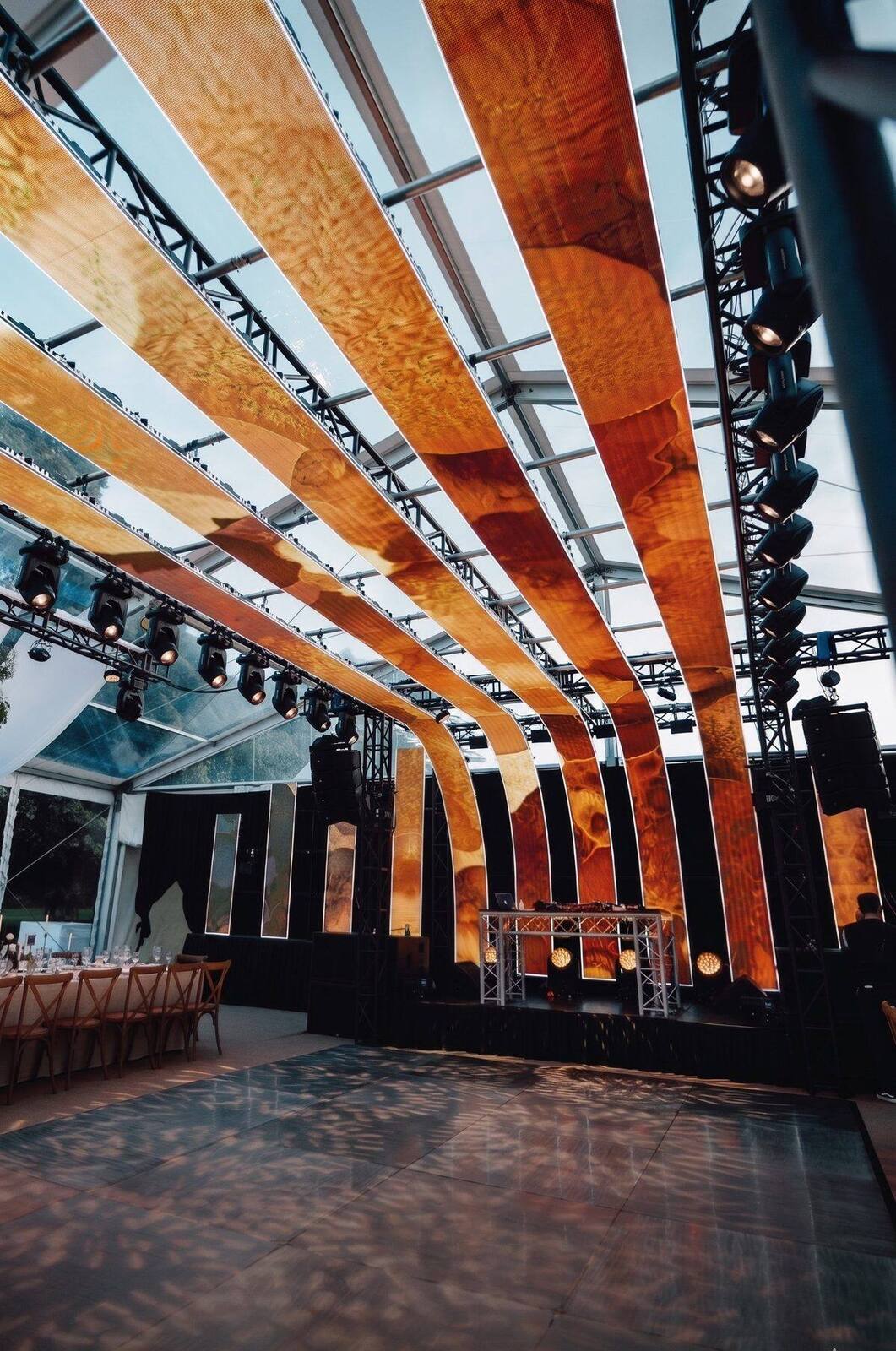 Pista de baile y cabina de DJ con diseño de iluminación cálida en carpa cristal para casamiento